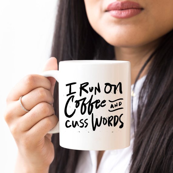 I Run On Coffee and Cuss Words coffee mug held by a person, showcasing a humorous design on a ceramic coffee mug.
