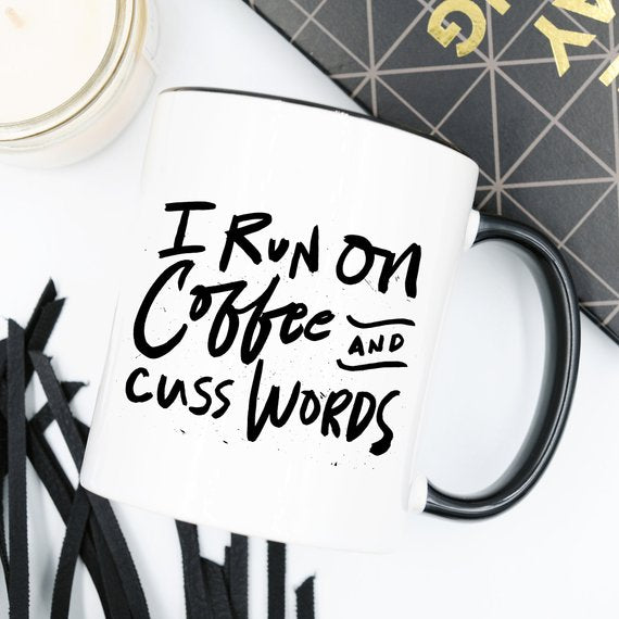 I Run On Coffee and Cuss Words coffee mug held by a person, showcasing a humorous design on a ceramic coffee mug.